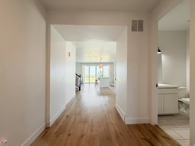 Hallway featuring wood-finish flooring, white baseboards, and a framed doorway opening to a kitchen with an island and a bathroom with a white vanity