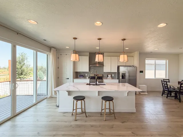 Open-concept kitchen featuring a large island with a light-toned countertop, stainless steel appliances, pendant lighting, and wood-finish flooring