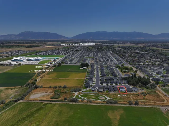 Aerial perspective showcasing a residential neighborhood with surrounding green fields and mountainous backdrop