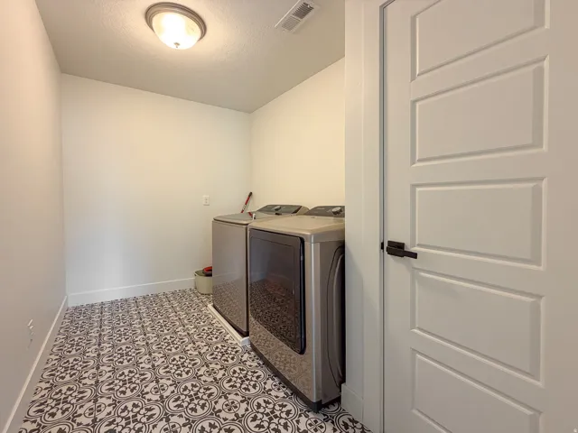 Utility room featuring patterned tile flooring, a flush-mount ceiling light fixture, white baseboards, and a paneled interior door with matte black hardware