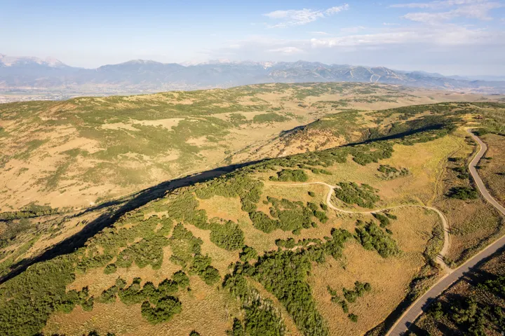 Sweeping aerial landscape featuring extensive natural terrain, a winding paved road, and a distant mountainous horizon