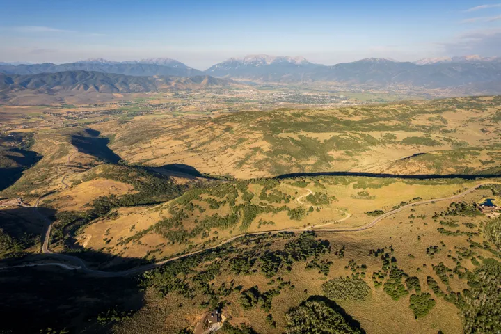 Expansive mountain landscape featuring varied terrain, a winding road, distant city, and snow-capped peaks