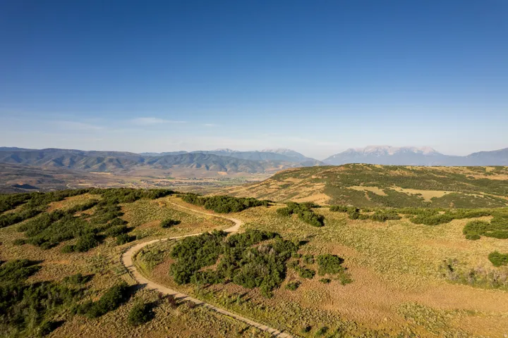 Expansive undeveloped land featuring a winding dirt road and extensive ground cover, set against a backdrop of distant mountains