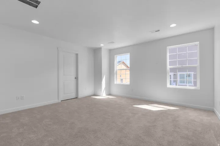 Spacious room with light-colored carpeting, white walls, two white-framed windows, recessed lighting, and a white interior door