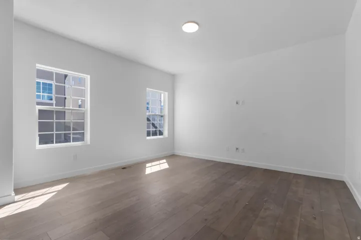 Spacious room with wood-finish flooring, white walls, and two multi-pane windows