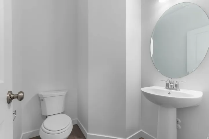 Powder room featuring a pedestal sink, oval mirror, and wood-finish flooring
