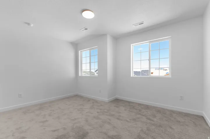 Light-filled room featuring two multi-pane windows, neutral-toned carpeting, white walls, and a ceiling-mounted light fixture