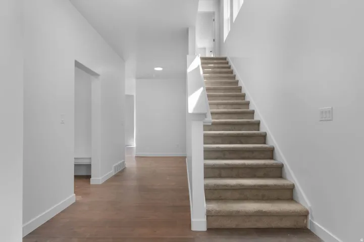 Carpeted staircase featuring white balusters and a wood-finish handrail, complemented by bright white walls and wood-finish flooring