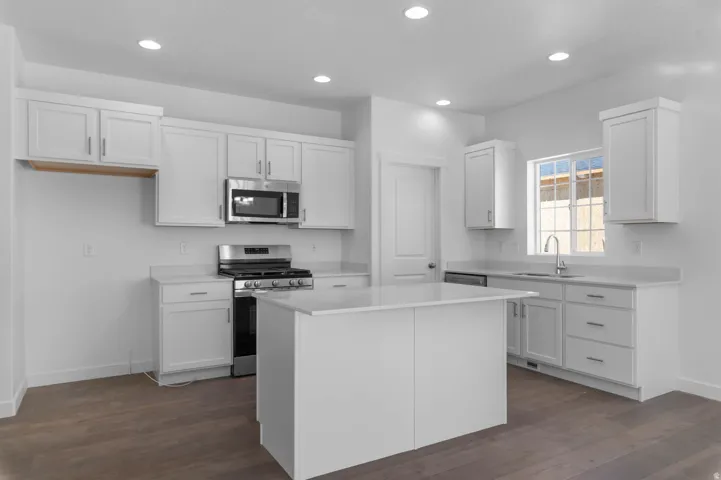 Modern kitchen featuring white shaker cabinetry, stainless steel appliances, a center island, and wood-finish flooring