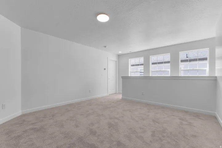 Carpeted loft space featuring a white painted half-wall, three multi-pane windows, a flush-mount ceiling light, and white baseboards