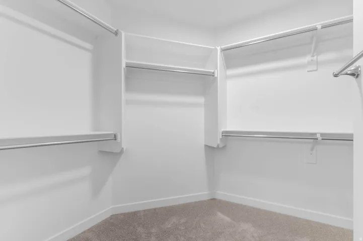 Walk-in closet with ample storage, featuring integrated shelving, multiple hanging rods, and neutral-toned carpeting