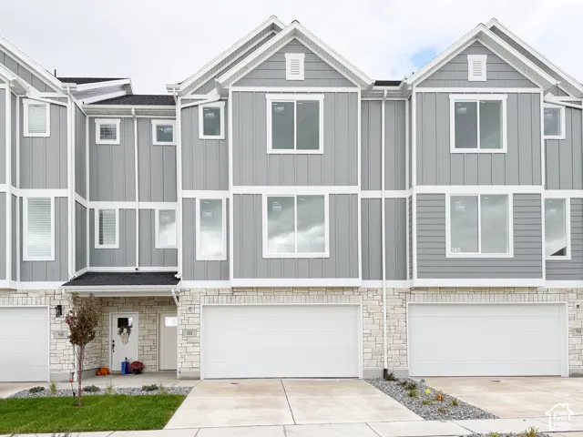 Multi-story townhouse exterior featuring gray vertical siding, stone veneer masonry on the lower level, dual-pane windows, and attached two-car garages