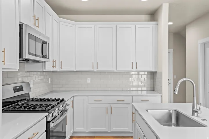 Contemporary kitchen featuring white cabinetry, light-toned countertops, a stainless steel gas range, and a subway tile backsplash