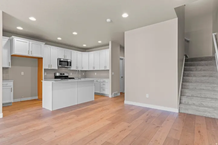 Open-concept kitchen and living area featuring wood-finish flooring, white cabinetry, a kitchen island with sink, stainless steel appliances, and recessed lighting