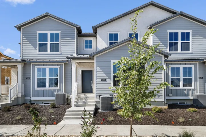 Modern townhome exterior featuring light gray horizontal siding, white trim, a dark gray entry door, and a contrasting light stucco upper facade