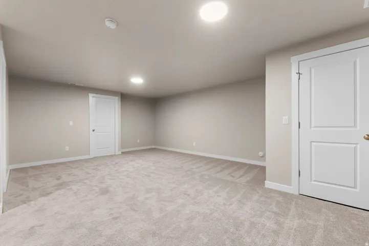 Spacious room featuring light-colored carpeting, neutral wall tones, two paneled doors, white baseboards, and recessed ceiling lighting