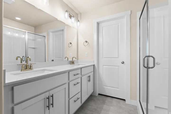Double vanity with white cabinetry, light-toned countertops, and brushed brass fixtures
