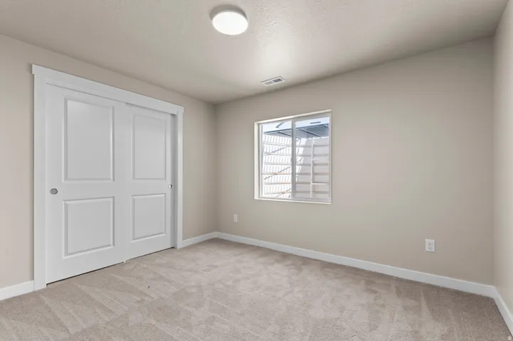 Room with neutral-toned walls, light-colored carpeting, a window featuring a window well, and white bi-fold closet doors
