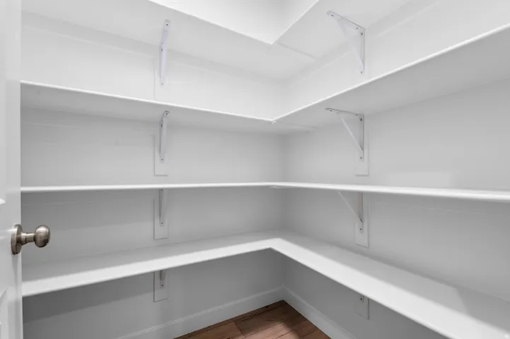 Walk-in pantry featuring white shelving, white walls, and wood-finish flooring
