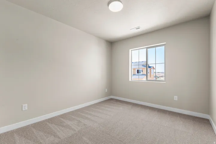 Carpeted interior room featuring a large window, neutral wall tones, white trim, and a ceiling-mounted light fixture