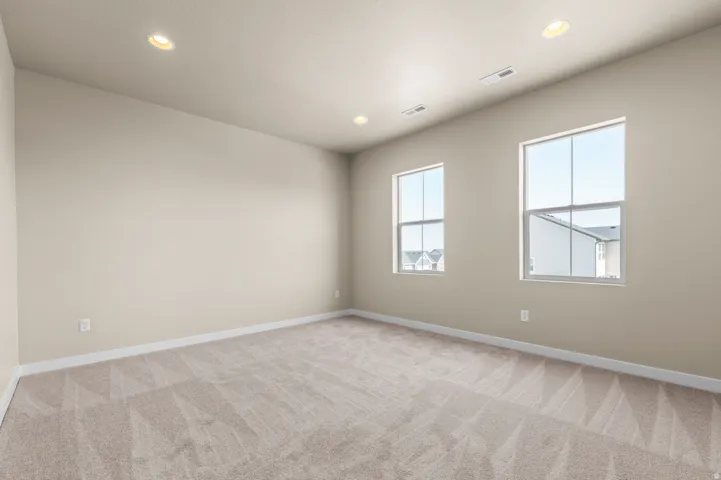 Spacious room featuring neutral carpeting, light-toned wall paint, two double-hung windows, white baseboards, and recessed ceiling lighting