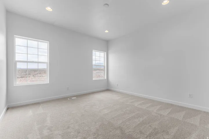 Spacious room featuring neutral carpet flooring, white walls, two grid-pattern windows, and recessed ceiling lighting
