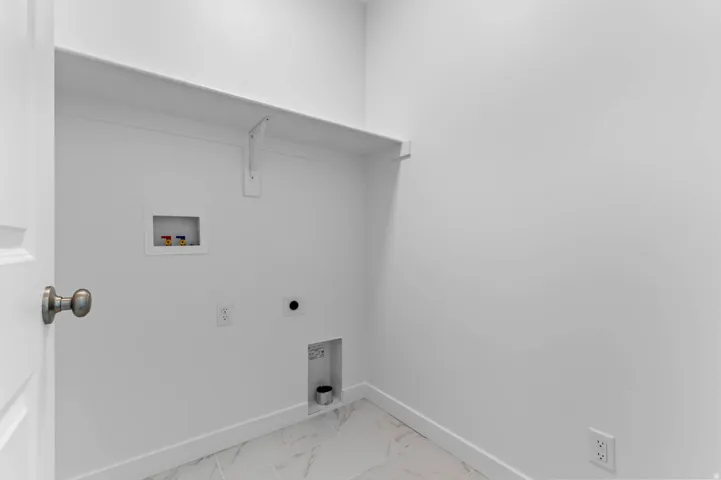 Dedicated laundry space featuring a white wall shelf, utility hookups, and marble-look floor tiles