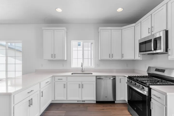 Modern kitchen featuring white shaker cabinetry, light-toned countertops, and stainless steel appliances, including a range with an overhead microwave and a dishwasher