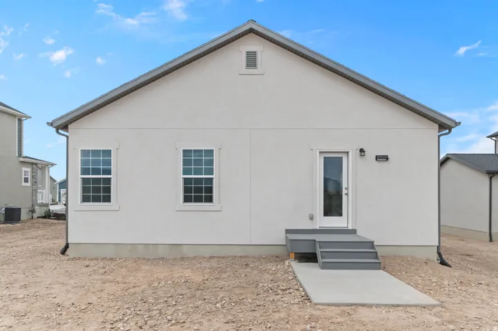 Rear exterior featuring light stucco siding, a grey pitched roof, and a white glass-paneled door