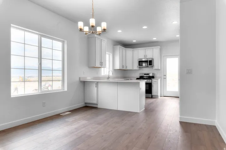 Open-concept kitchen and dining area featuring light wood-finish flooring, white cabinetry, stainless steel appliances, and a central island with a countertop