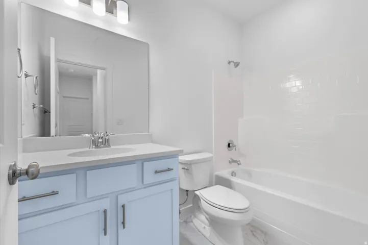 Bathroom featuring a light blue vanity, integrated sink, large wall-mounted mirror, three-light vanity fixture, and a white tub with subway tile surround