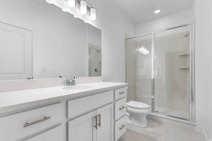 Bathroom featuring a single vanity with a white countertop and white cabinetry, a large frameless mirror, a chrome three-light fixture, a glass-enclosed shower, and a white toilet
