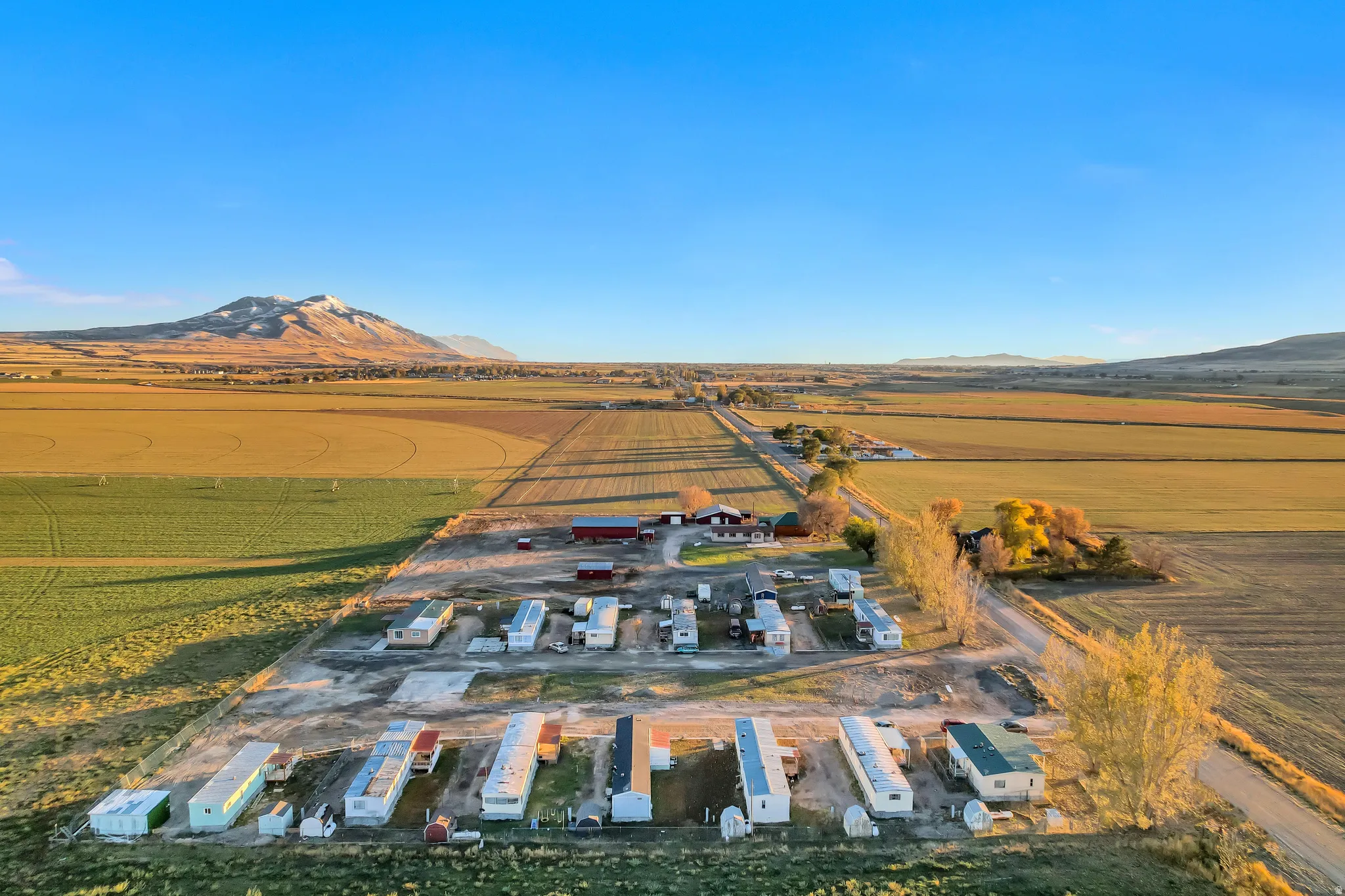 Expansive rural property featuring multiple manufactured homes, agricultural fields, distant mountains, and a clear sky
