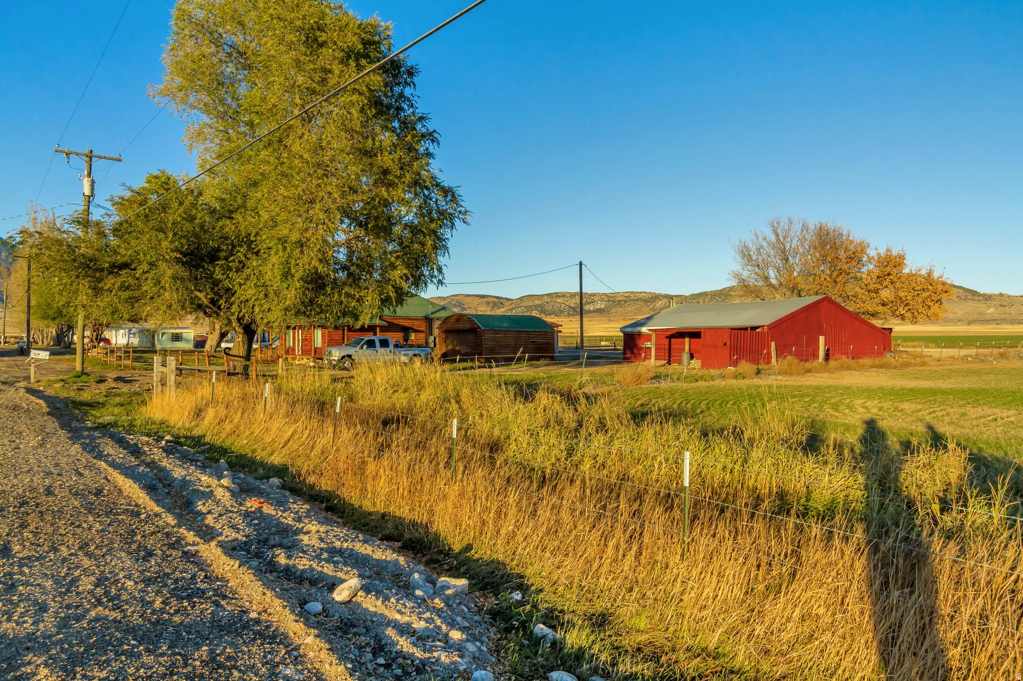 Expansive rural property featuring a red barn with a metal roof, mature trees, and a gravel road frontage