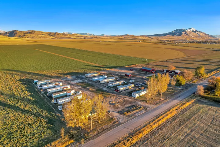 Expansive rural property featuring multiple manufactured homes, agricultural fields, a paved road, and distant mountain ranges