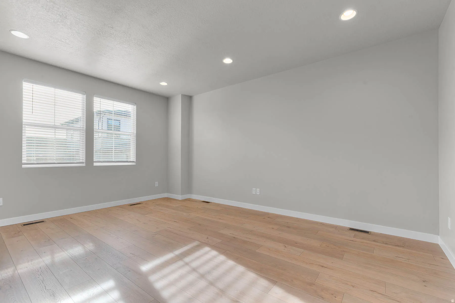 Expansive room featuring wood-finish flooring, recessed lighting, two windows with blinds, light gray wall paint, and white baseboards