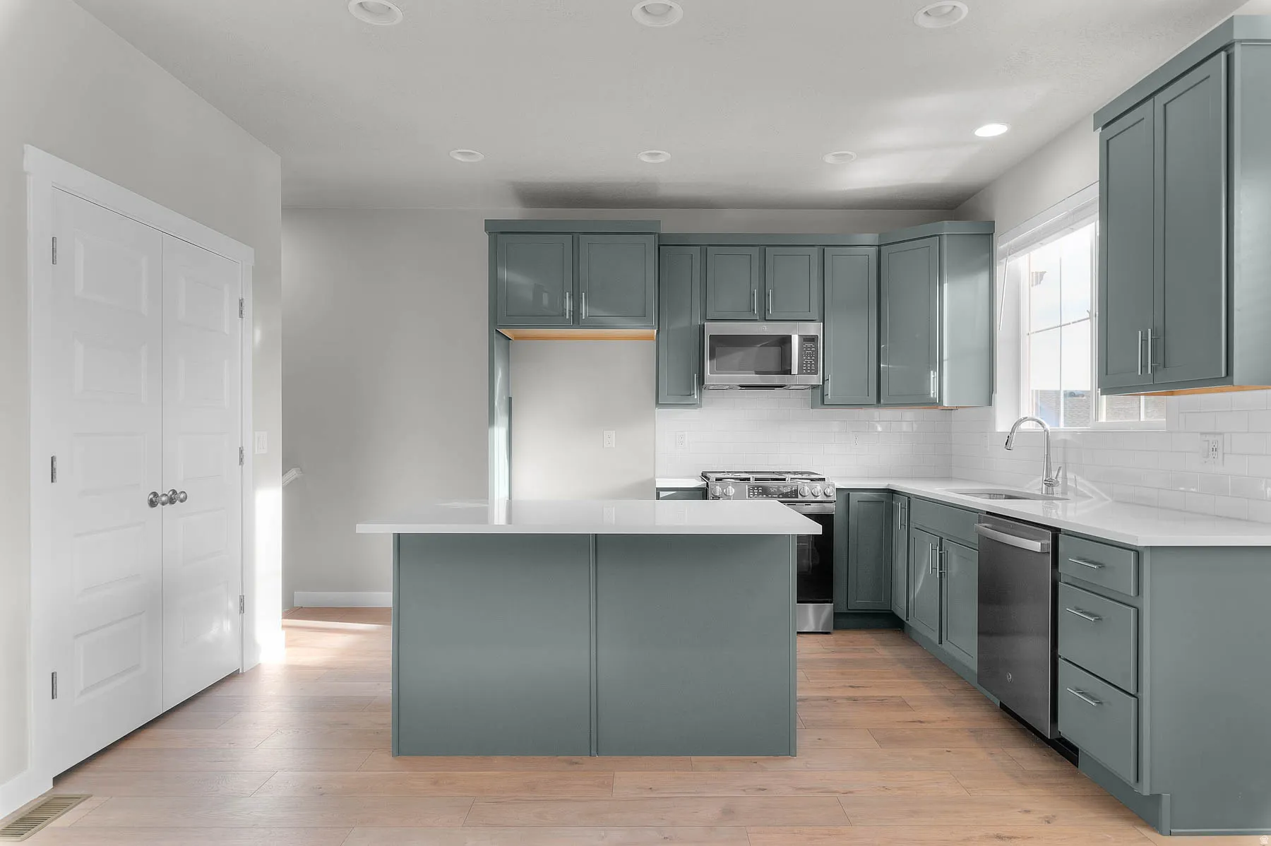 Modern kitchen featuring light wood-finish flooring, an island with a white countertop, and gray shaker-style cabinetry