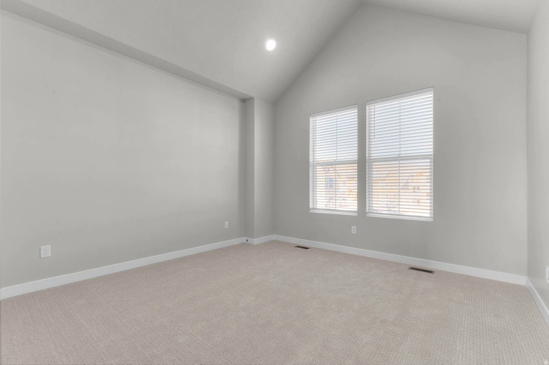 Spacious room featuring vaulted ceilings, light neutral wall paint, and plush carpeting