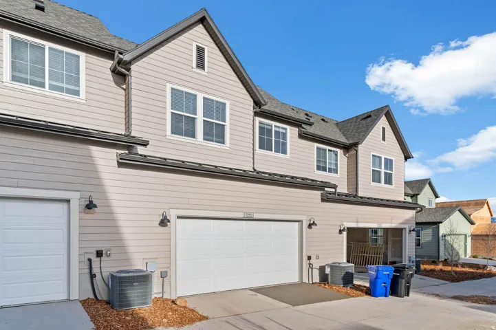 Multi-level townhome exterior featuring light-colored horizontal siding, dark roof shingles, and white-framed windows