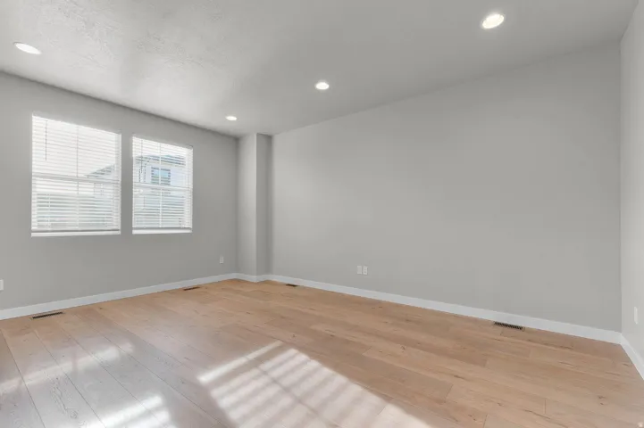 Expansive room featuring wood-finish flooring, recessed lighting, two windows with blinds, light gray wall paint, and white baseboards
