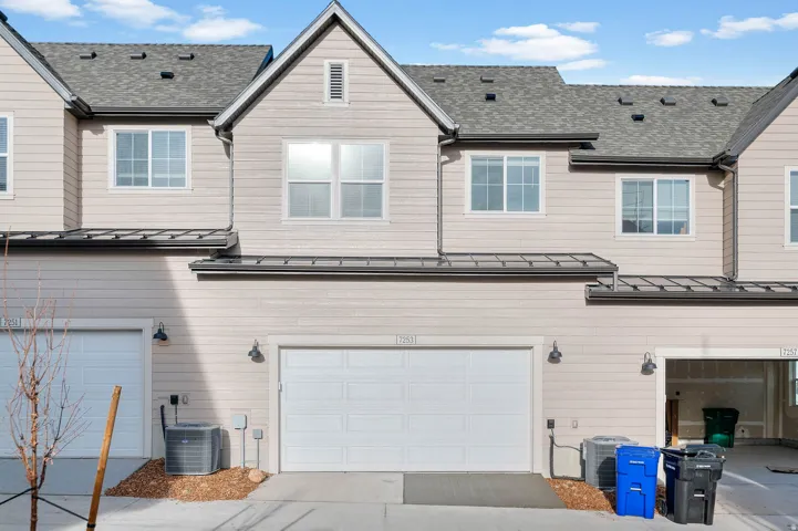 Exterior featuring horizontal siding, multiple windows, an attached garage, a gray shingle roof, and exterior lighting fixtures