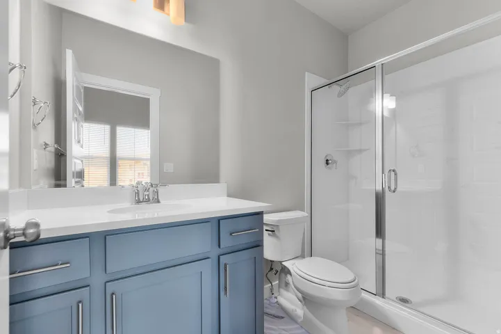 Bathroom featuring a vanity with blue cabinetry and white countertop, undermount sink, chrome faucet, and a shower with a sliding glass door