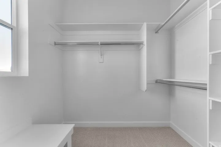 Walk-in closet featuring built-in shelving, multiple hanging rods, a window, a built-in bench, and carpet flooring