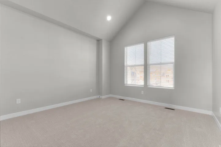 Spacious room featuring vaulted ceilings, light neutral wall paint, and plush carpeting