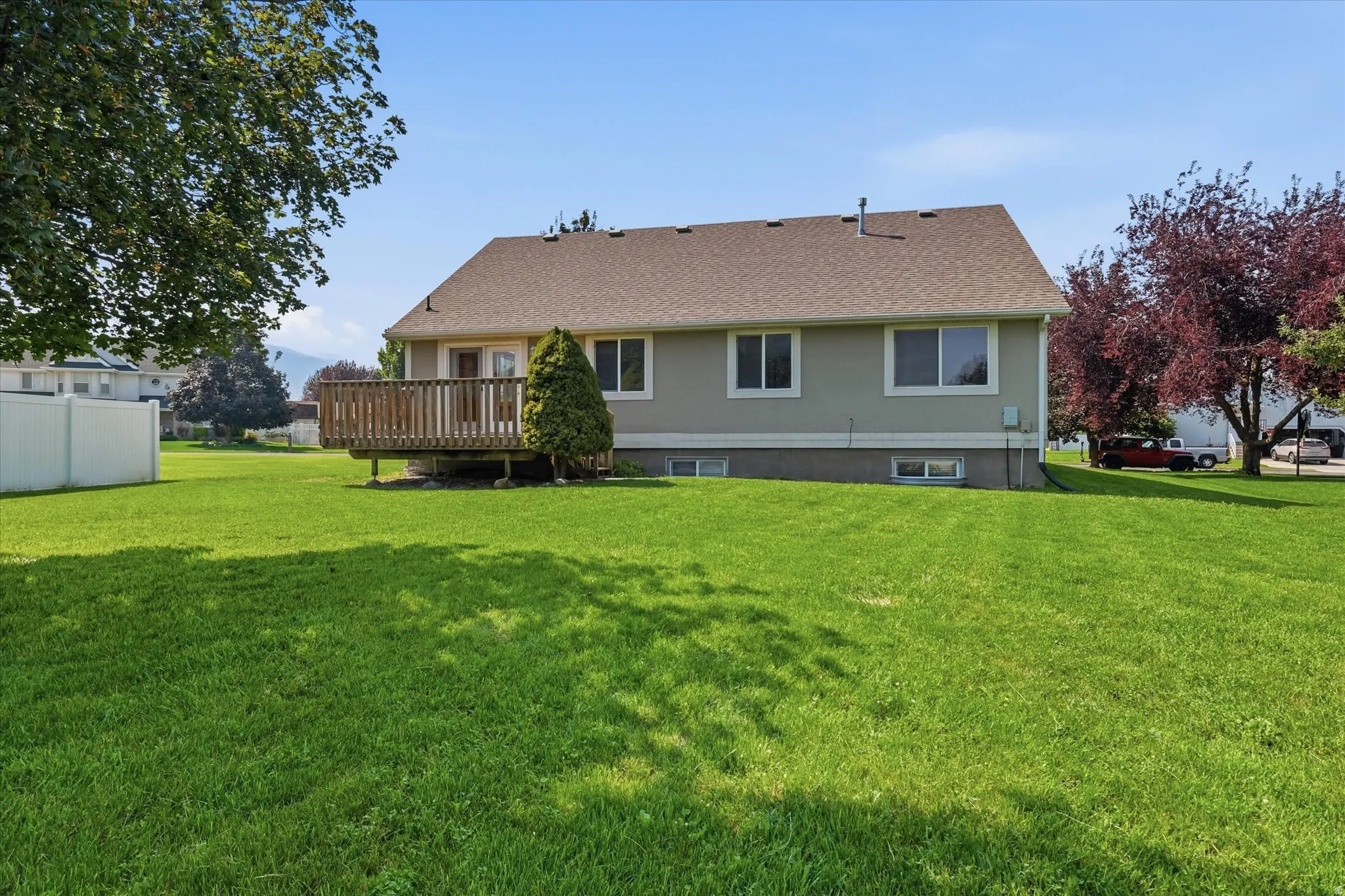 Expansive green lawn with a white vinyl fence, mature trees, and a wooden deck with railing