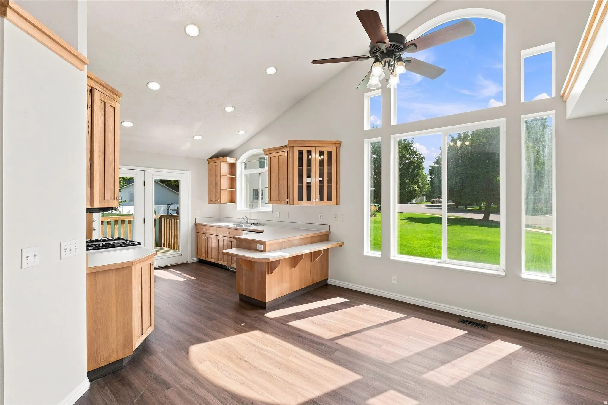 Vaulted ceiling with recessed lighting, wood-finish flooring, full wall of windows with arched transom, wood cabinetry, and a gas range