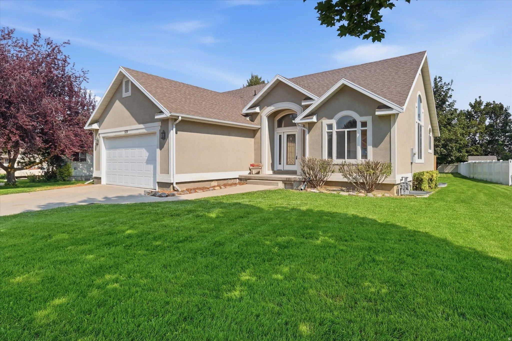 Stucco exterior with arched windows, an attached two-car garage, front entry with transom window, and a gabled roof