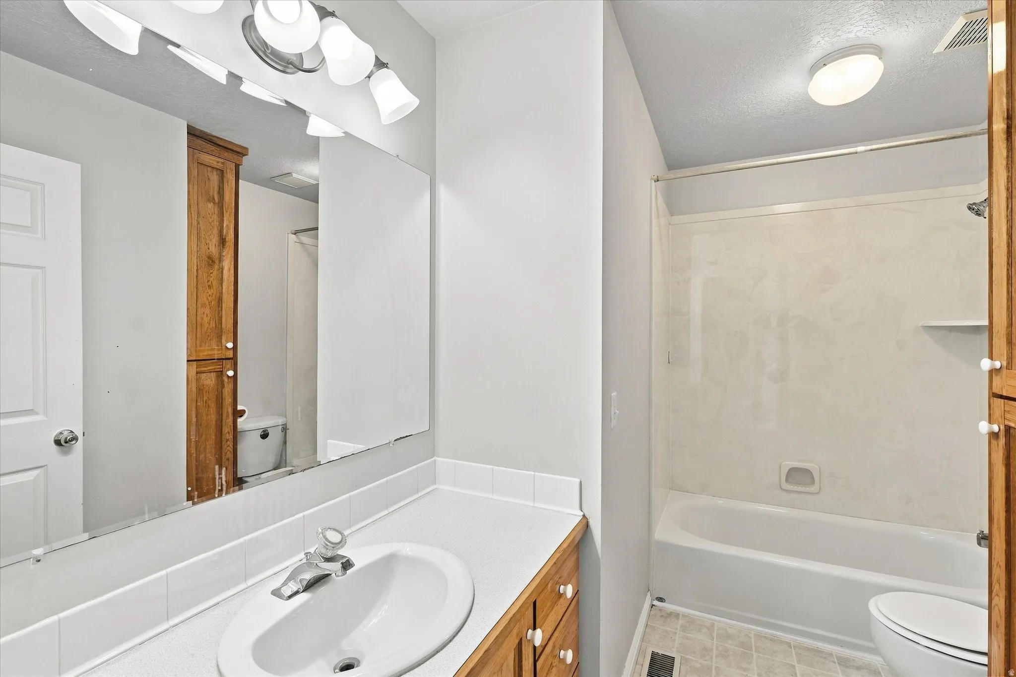Bathroom featuring a vanity with an integrated sink, a built-in wood-finish cabinet, a full-width mirror, and a tub-shower combination with a built-in shelf