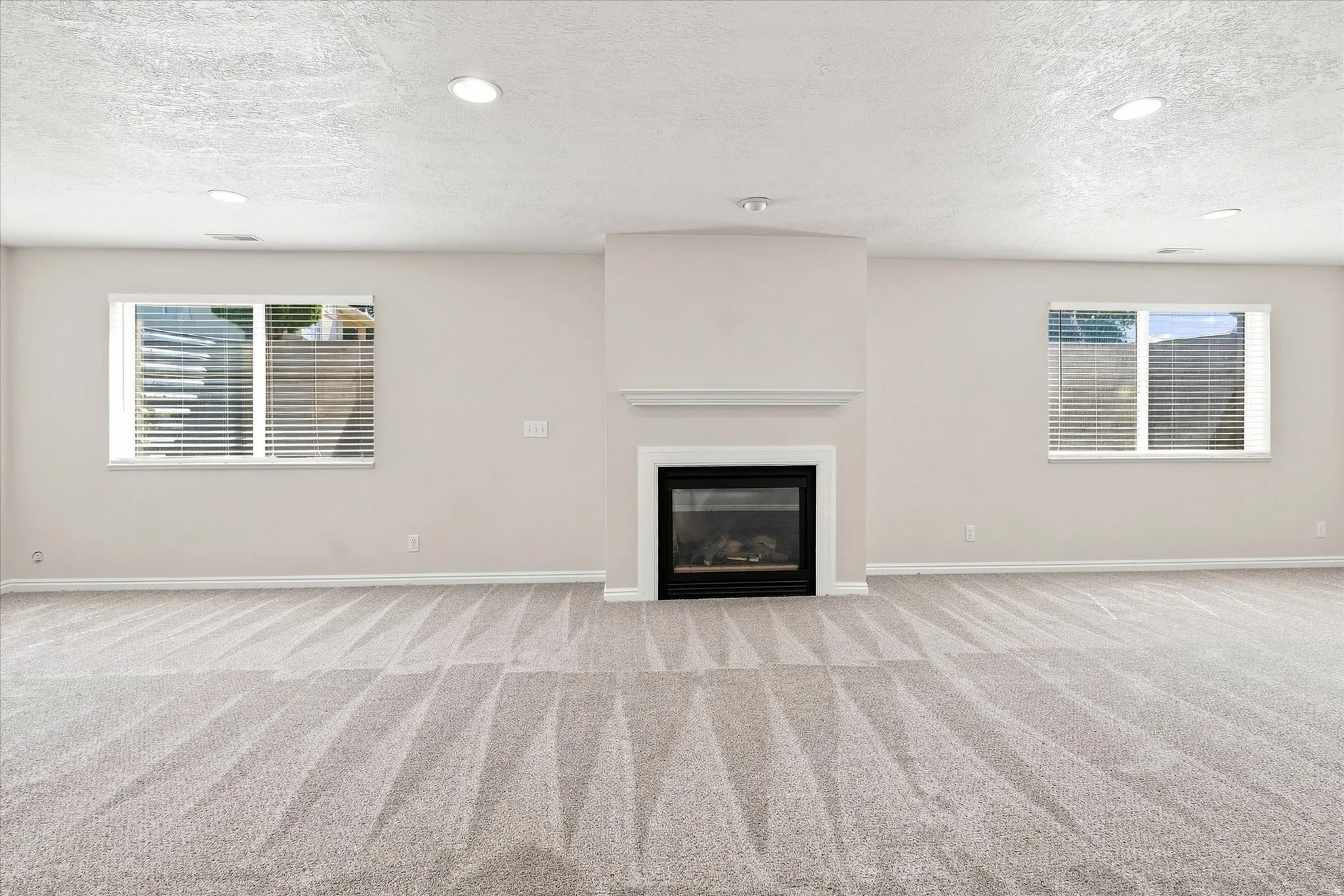 Spacious room featuring a central fireplace with a white mantel, recessed lighting, two windows, and light-toned carpeting