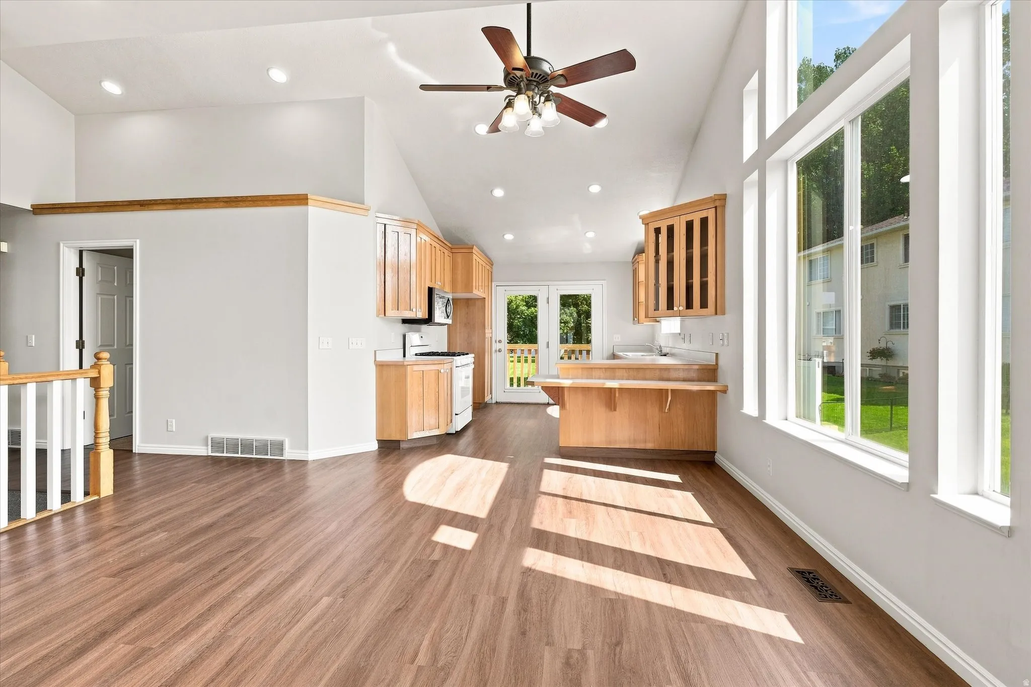 Vaulted ceilings, wood-finish flooring, kitchen with light wood cabinetry, built-in breakfast bar, and expansive windows
